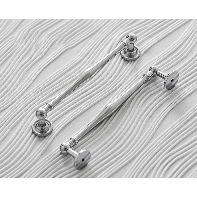Twee glanzende chromen meubelgrepen op stijlvol, golvend wit oppervlak, Aurel luxery hardware