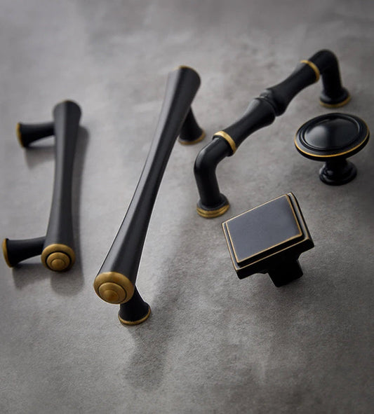 Mat zwarte en goudkleurige kastknoppen en grepen van Aurel luxury hardware op grijze ondergrond.